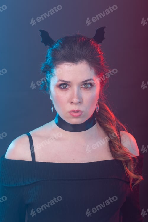Preview: Dark fashion, halloween and people concept - gothic woman in bat ears over the dark background