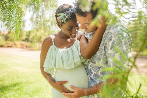 Preview: Happy diverse pregnant couple hugging and caressing belly in park