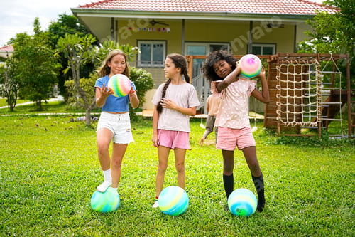 Preview: Three children have fun bouncing colorful balls in a vibrant backyard under bright sunshine
