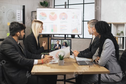 Preview: Focused multiracial business people in conference room, looking at a laptop, having video conference