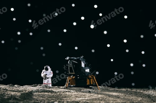 Preview: Astronaut miniature toy next to a spaceship on the moon against bokeh background