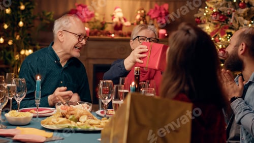 Preview: Excited husband giving his wife present while enjoying Christmas dinner with relatives