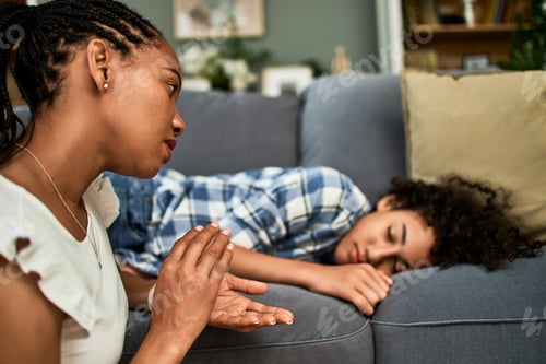 Preview: Mother waking up teenage son who is asleep on a couch in a living room.