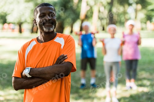 Preview: selective focus of cheerful african american man standing with crossed arms near pensioners