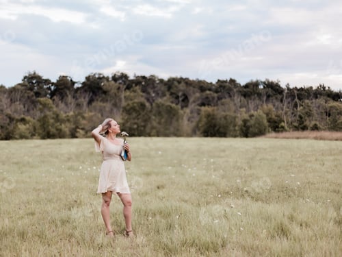 Preview: Young blonde millennial woman outdoors in field holding blue hardcover book, earth tone colors