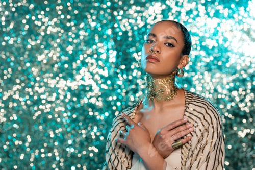 Preview: african american woman with piercing and gold on neck posing with crossed arms on sparkling blue