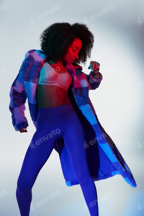 Preview: alluring stylish african american female model in fashionable faux fur looking way in lights