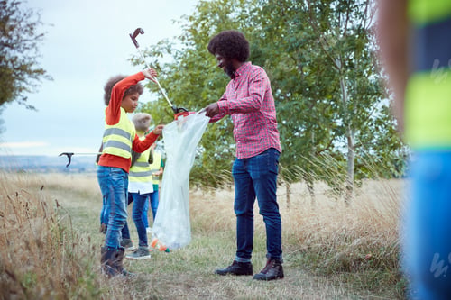 Preview: Adult Team Leader With Group Of Children At Outdoor Activity Camp Collecting Litter Together