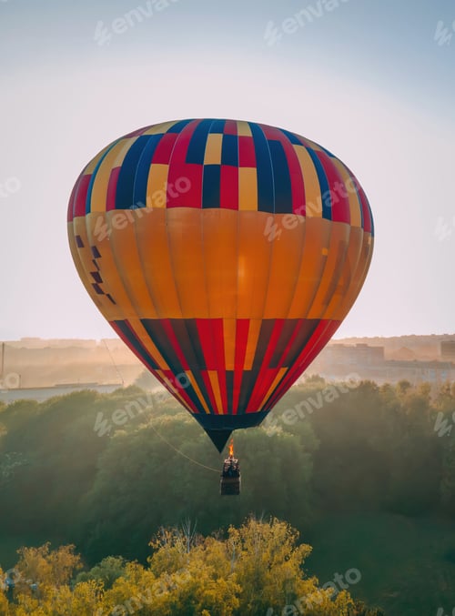 Preview: Colorful hot air balloon takes off from green park in small european city at summer sunrise