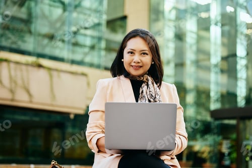 Vista previa: Empresaria asiática sonriente trabajando en un ordenador portátil al aire libre y mirando a la cámara.