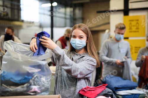 Preview: Volunteers sorting out donated clothes in community charity donation center, coronavirus concept.