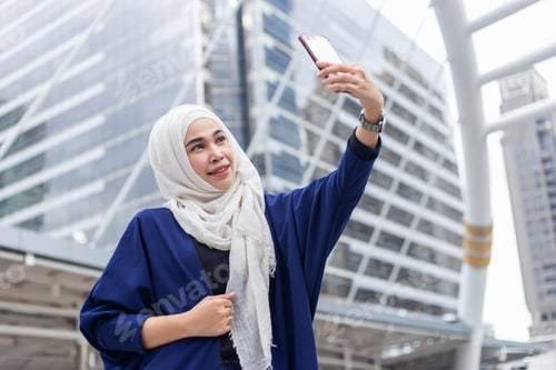 Preview: young muslim attractive woman in hijab making selfie photo on smartphone