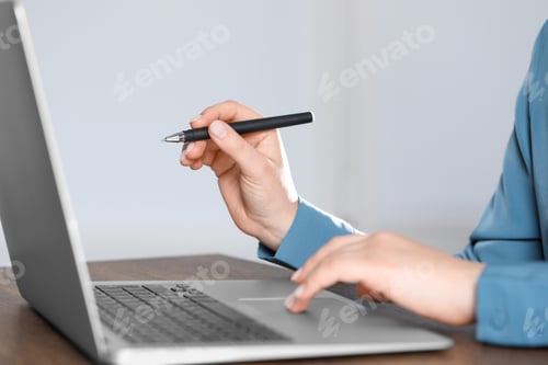 Preview: Woman with pen working on laptop, closeup. Electronic document management