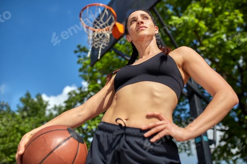 Preview: Beautiful, sporty latin girl with a basketball under the ring on a street basketball court. Sport