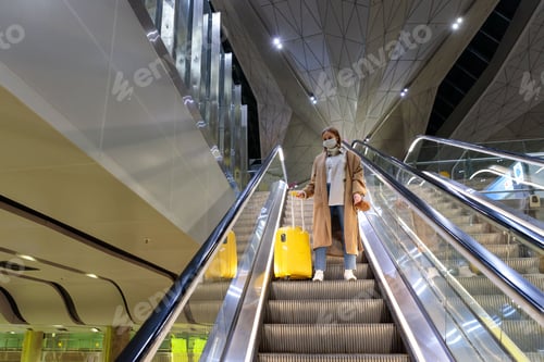 Preview: Woman with yellow luggage stands on escalator at empty airport due to coronavirus pandemic