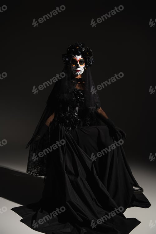 Preview: full length of woman in black dress with veil and spooky halloween makeup sitting on black