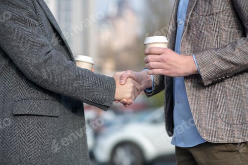 Preview: Two men with coffee cups shaking each others hand