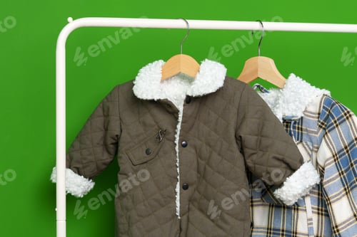 Preview: Two kids winter coats hanging on hangers against green wall in studio
