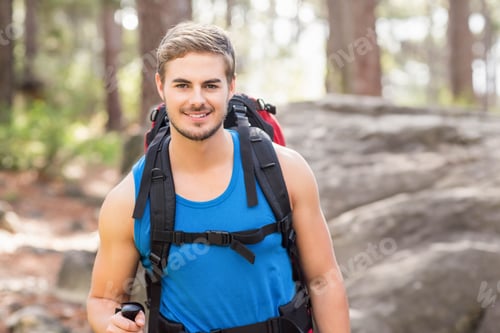 Preview: Man hiking on wooded trail wearing blue tank top holding trekking pole and carrying backpack