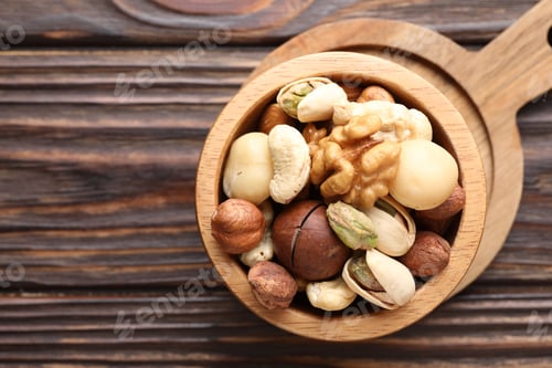 Preview: Mix of different nuts in bowl on wooden table, top view. Space for text
