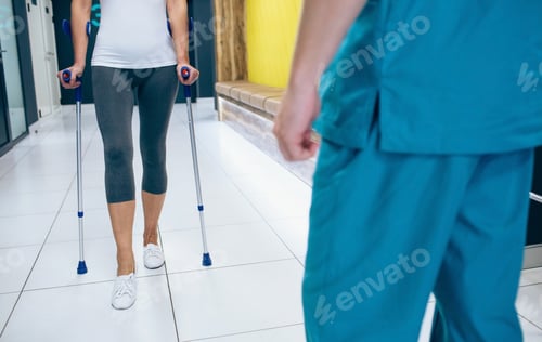 Preview: Woman patient using crutches for rehabilitation after injury. Physiotherapist assisting a patient.