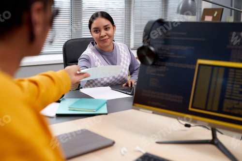 Preview: Two young people working in IT development and handing documents across table