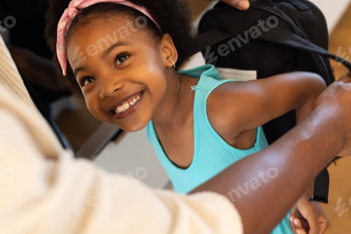 Preview: Smiling girl wearing backpack, getting ready for school with parent's help