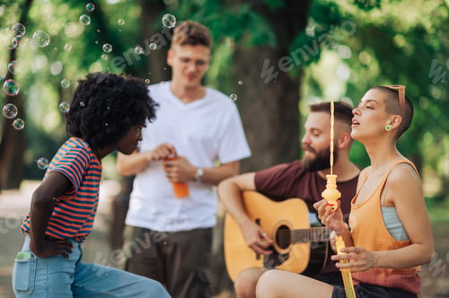 Preview: Four friends are spending time together in park and relaxing with guitar.