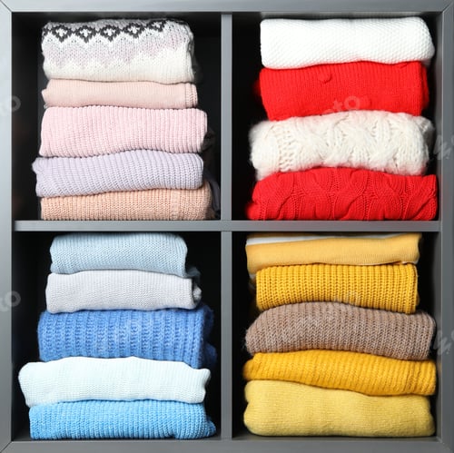 Preview: Many knitted winter clothes stacked on shelves near white background