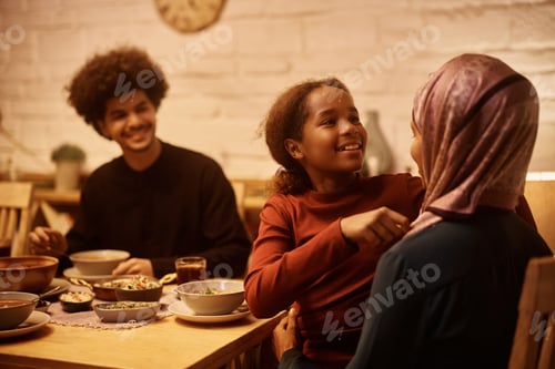 Preview: Happy Muslim mother and daughter talking during family dinner at dining table.