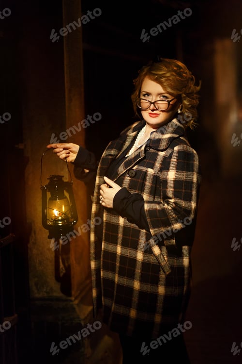 Preview: Mysterious blonde woman in elegant retro coat with old oil lantern walking in old street