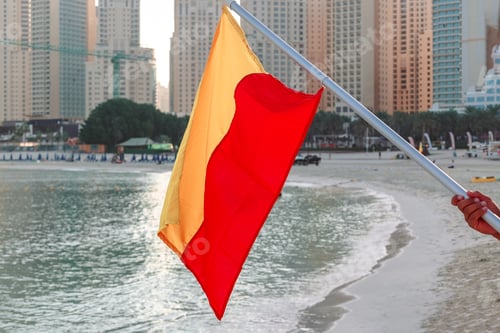 Preview: Man's hands holding flag of Poland on beach over sea water