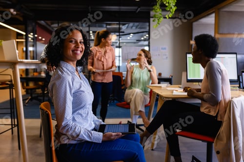 Preview: Portrait of happy biracial casual businesswomen holding tablet in office