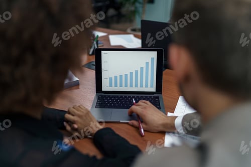 Preview: Two businesspartners working together in modern coworking and looking laptop. Back view