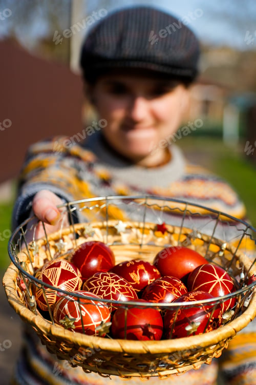 Preview: Closeup of basket of colored red eggs, Easter holiday concept. Young person holding modern painted e