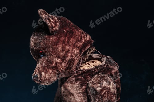 Preview: Old brown teddy bear with its head torn off on a black background