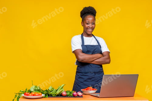 Preview: African female chef posing in front of a yellow wall