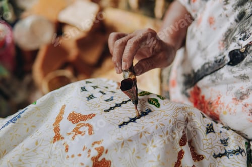 Preview: Close up picture of a person's hand drawing the design pattern of Indonesian batik tulis fabric.