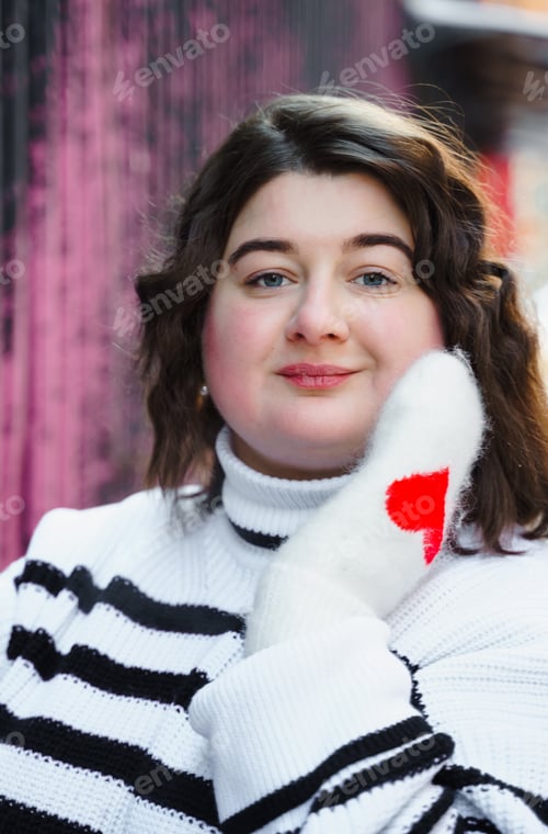 Preview: Smiling plus-size woman wearing a striped sweater with red heart details on sleeves. Standing