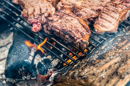 Preview: Pieces of steak on a grill over charcoal fire.
