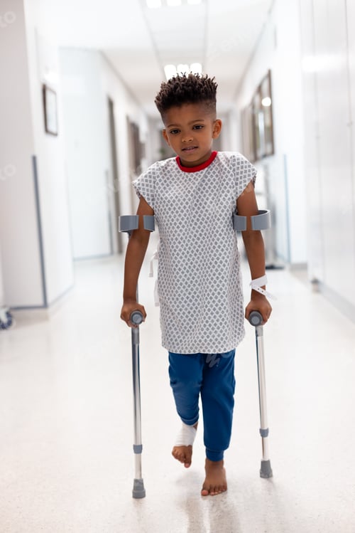 Preview: Vertical of african american boy patient walking with crutches in hospital corridor with copy space