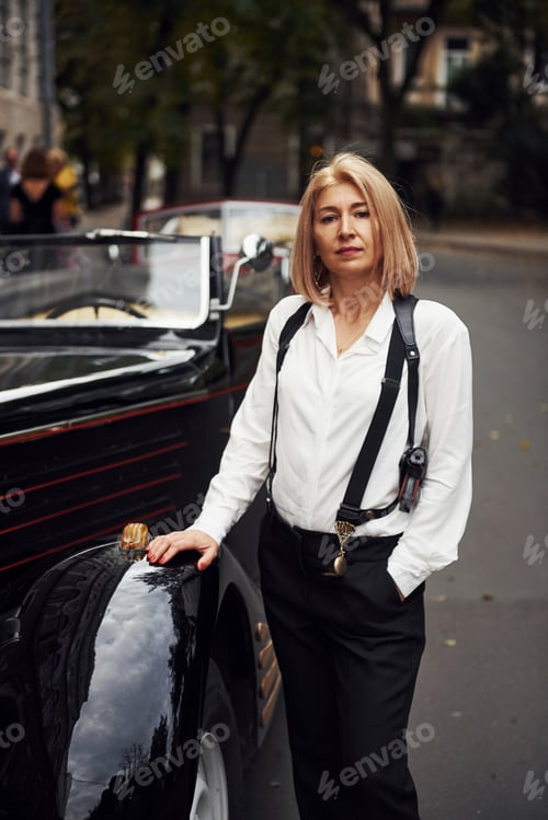Preview: Blonde woman in black retro clothes near old vintage classic car