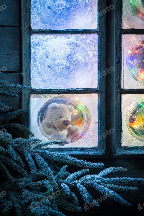 Preview: Teddy bear in frozen window for Christmas with tree and lights