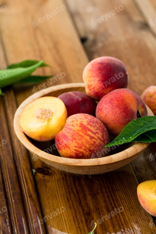 Preview: Peaches with leaves in a wooden bowl with peach in halves on top.juicy peaches. Harvest