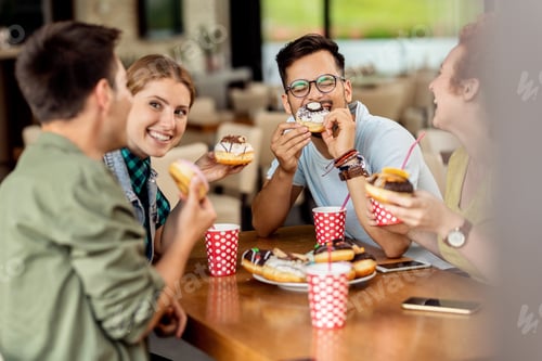 Preview: Carefree friends having fun while eating donuts and talking in a cafe.