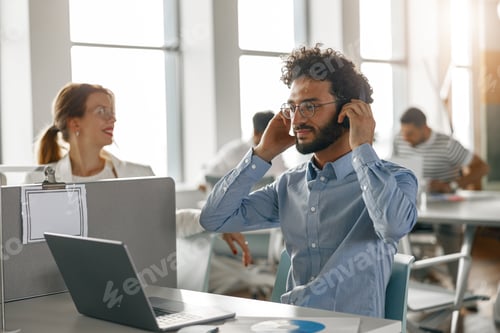 Preview: Businessman in headphones working laptop while sitting in modern office on colleagues background