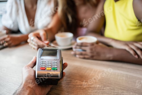Preview: Payment terminal and a girl using her credit card with her friends in a coffee shop