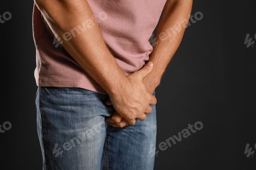 Preview: Man suffering from pain on black background, closeup. Urology problems