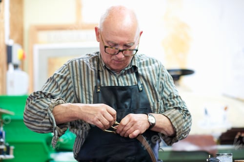 Preview: Male worker in leather workshop, polishing belt buckle