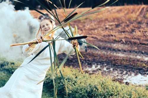 Preview: Happy woman in white dress with green smoke bomb and reeds dancing on muddy field